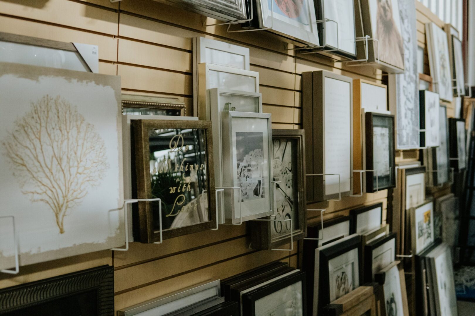 Many framed pictures on a wall in a store.
